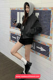 Person wearing a gray hoodie and black outfit against a tiled wall with colorful patterns.