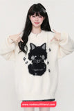 Person wearing a white sweater with a black cat design, pointing at the sweater.