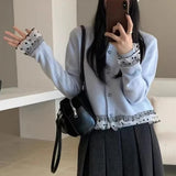 Person wearing a light blue cardigan with decorative trim, holding a black handbag indoors.