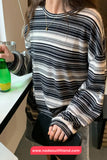 Person wearing a striped sweater sitting at a table with a drink, brand 'Nada Outfitland' visible.