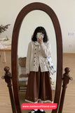Person wearing a white cardigan and brown pants standing in front of a full-length mirror.