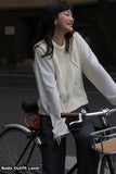 Woman in a white sweater and dark pants standing next to a bicycle, with a blurred background.