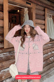 Woman wearing a pink sweater and gray hat in front of a wooden cabin.