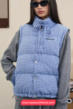 Person wearing a blue checkered puffer vest over a gray shirt with sunglasses, standing against a plain background.