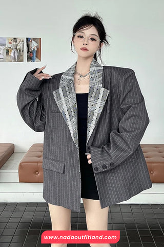 Person wearing a gray pinstripe blazer with a white shirt underneath, standing in a room with a couch and framed pictures on the wall.