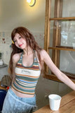 Woman in a striped tank top sitting at a table with a cup in a casual setting.
