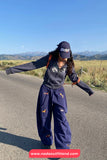 Person wearing a navy outfit with a cap, standing on a road with mountains in the background.