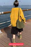 Person wearing a yellow sweater and black skirt with a green bag, standing on a boat deck.