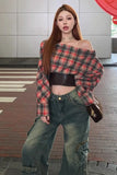 Woman wearing a plaid off-shoulder top and green pants on a city street.