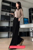 Woman in a beige blouse and black pants standing in an indoor setting with a modern interior.