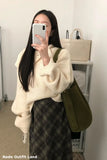 Person taking a mirror selfie wearing a cream sweater and plaid skirt with a green bag.