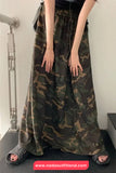 Person wearing a long camouflage skirt with a white wall background