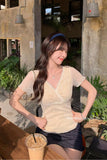 A woman posing in a beige lace short-sleeve V-neck top and a dark denim mini skirt at an outdoor cafe table with an iced coffee.