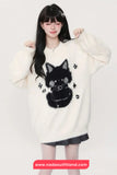 Person wearing a white sweater with a black cat design on a plain background