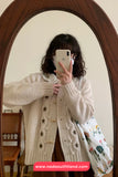 Person wearing a white cardigan with star patterns, holding a phone in front of a mirror.