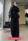 Person wearing a black outfit with a jacket and hijab, standing in a modern indoor setting.