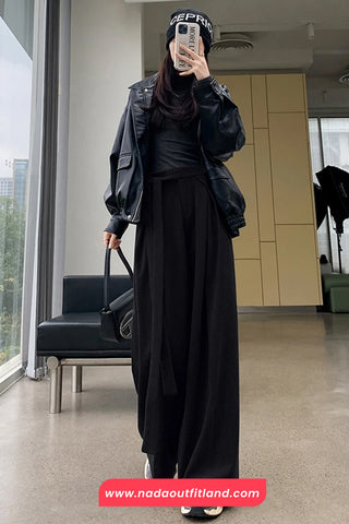 Person wearing a black outfit with a jacket and hijab, standing in a modern indoor setting.
